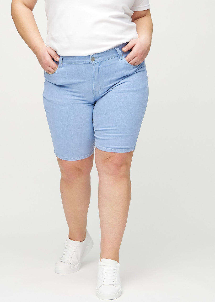 Ljusblå skinny middle shorts, modellnamn Skies, som sitter tätt över låret och slutar precis ovanför knät på en plus-size-modell, sett framifrån.