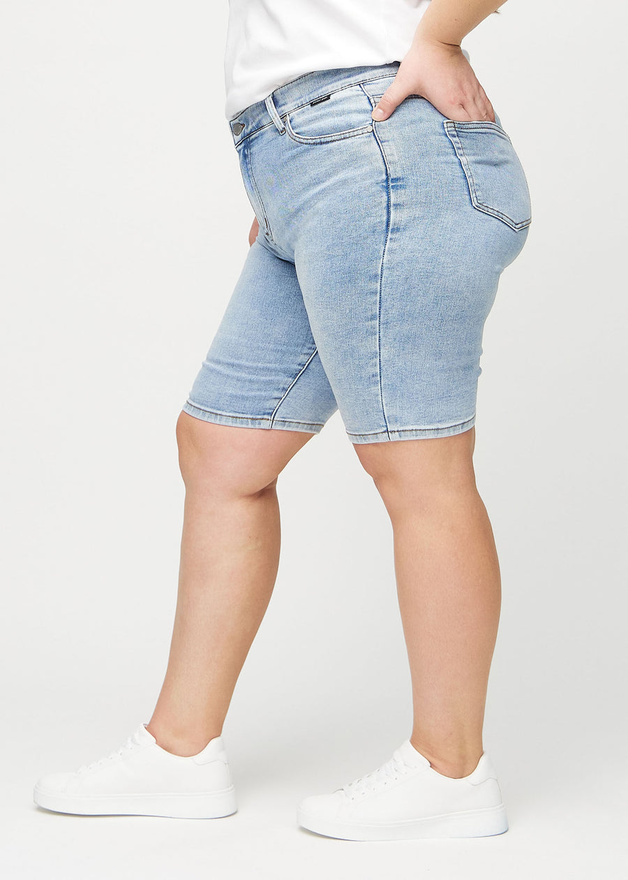 Ljus denim skinny middle shorts sedda från sidan på en plus-size-modell.