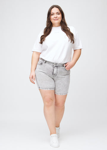 Helbild av en plus size-modell i ljusgrå denim skinny short shorts.
