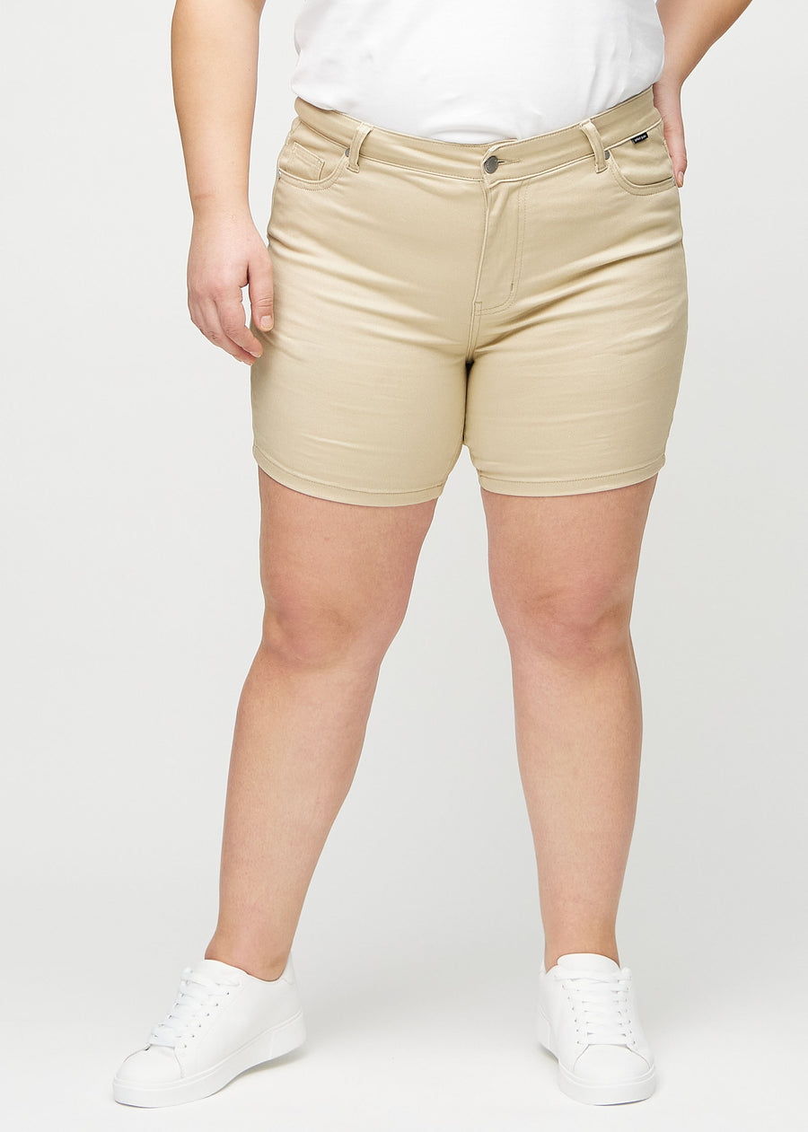 Beige skinny short shorts, modellnamn Gazelles, som sitter tajt och slutar mitt på låret på en plus-size-modell, framifrån.