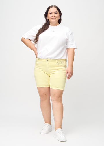 Helbild av en plus-size-modell i ljusgula skinny short shorts.