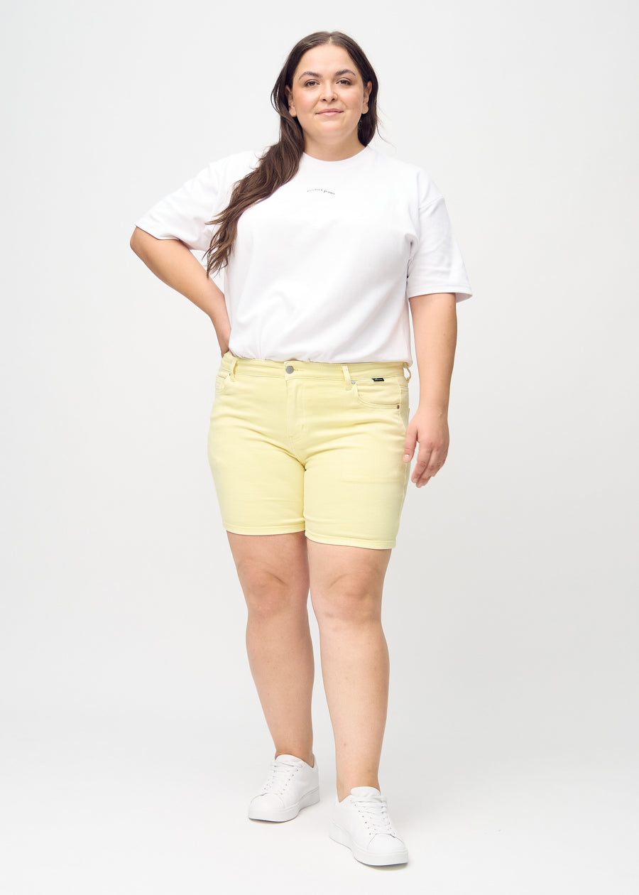 Helbild av en plus-size-modell i ljusgula skinny short shorts.