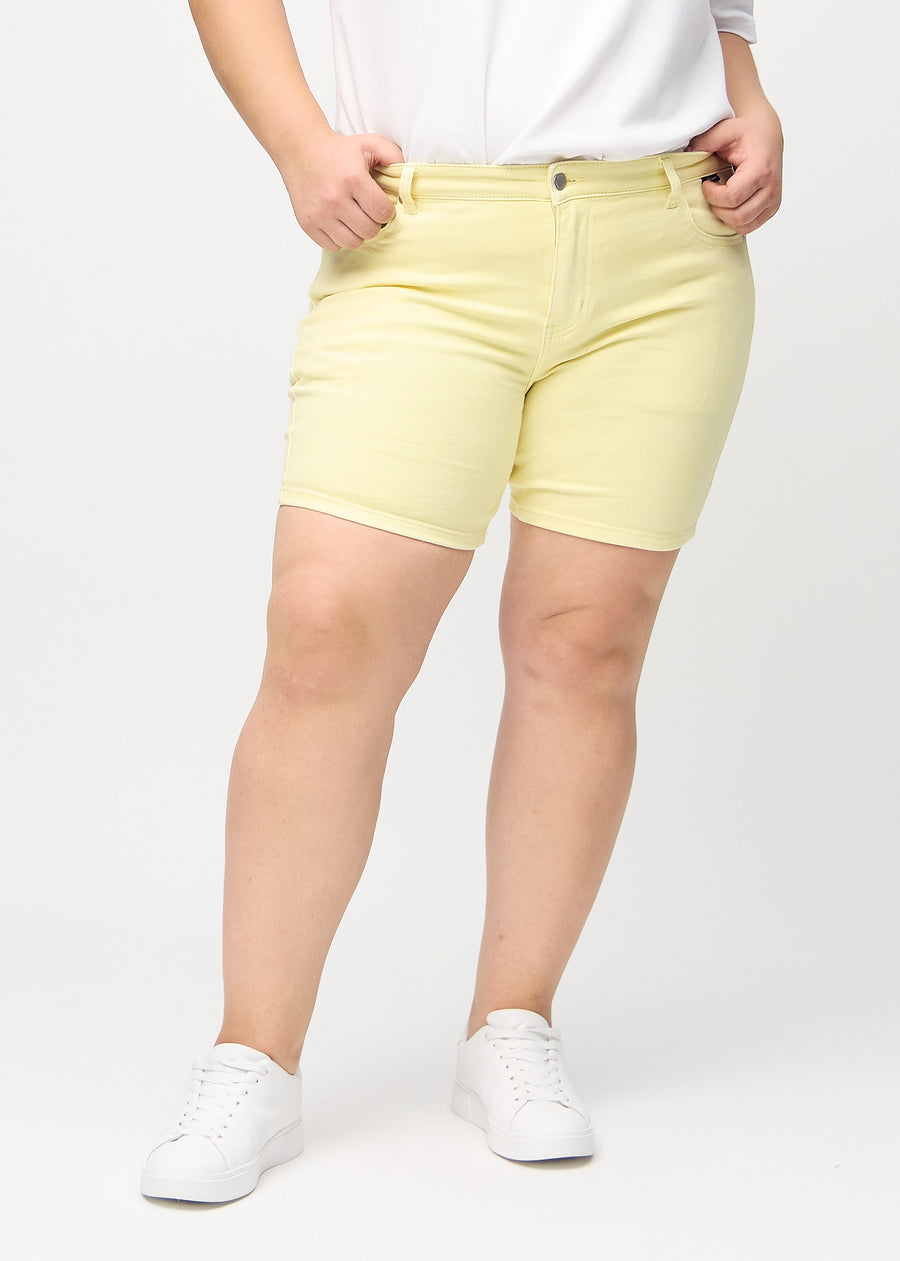 Ljusgula skinny short shorts, modellnamn Lemonades, som sitter tight och slutar mitt på låret på en plus-size-modell, sedda framifrån.