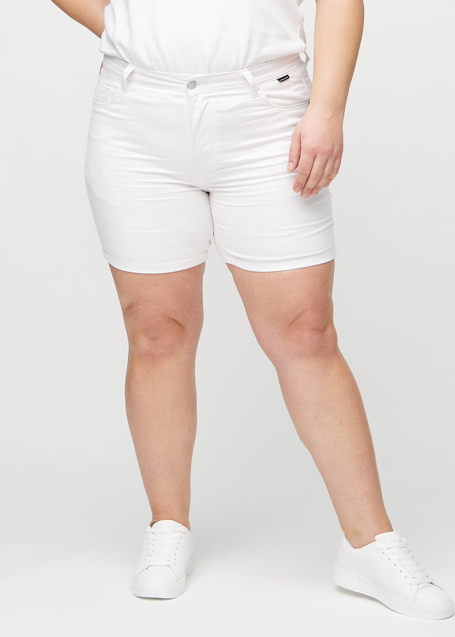 Vita skinny short shorts, modellnamn Marguerites, som sitter tajt och slutar mitt på låret på en plus size-modell, sedda framifrån.