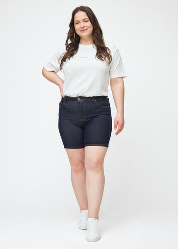 Helbild av plus-size modell i mörkblå denimshorts för dam i färgen Midnights med skinny passform.