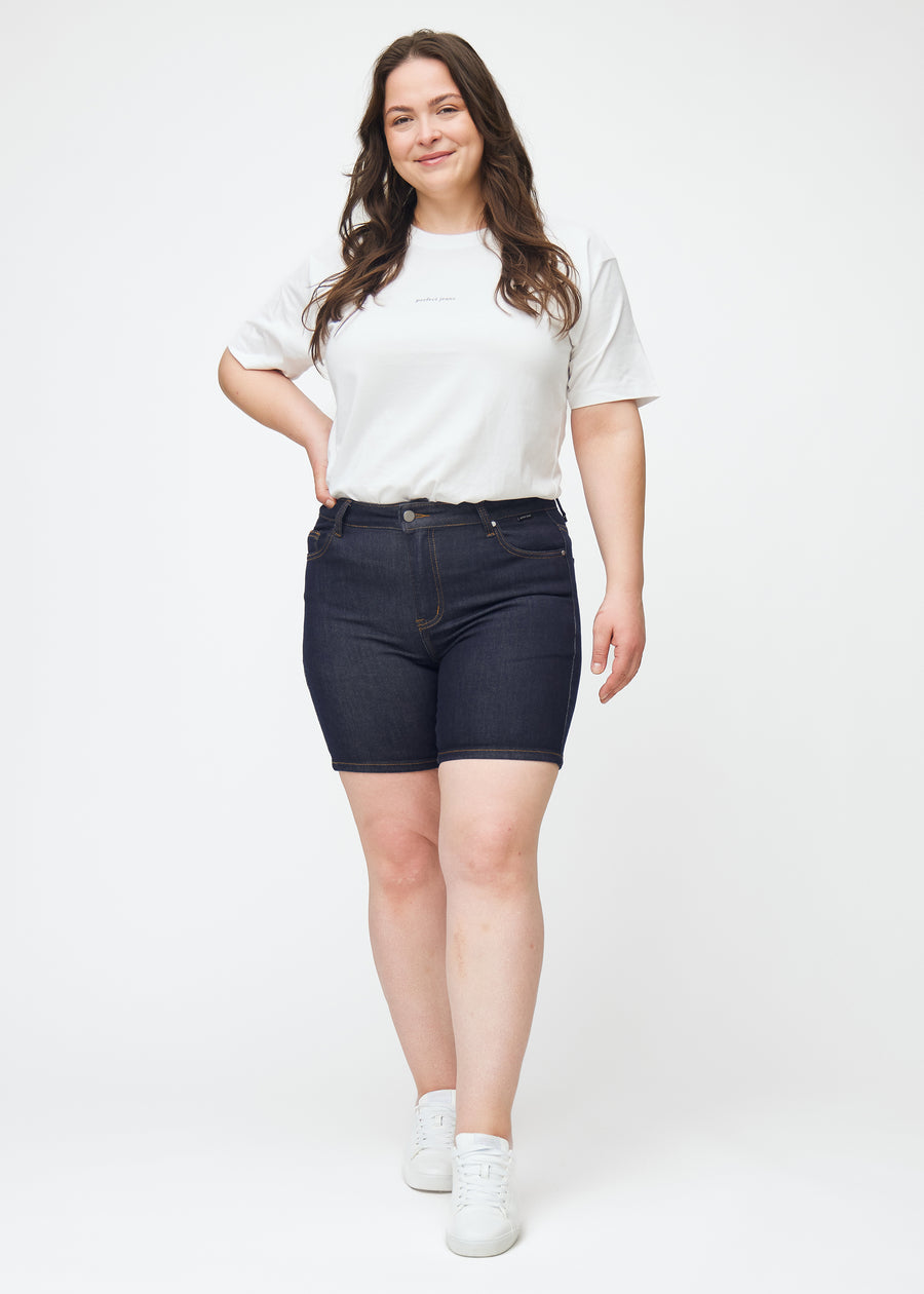 Helbild av plus-size modell i mörkblå denimshorts för dam i färgen Midnights med skinny passform.