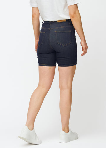 Mörkblå denimshorts för dam i färgen Midnights sett bakifrån, där den åtsittande passformen och längden till mitten av låret syns.
