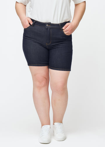 Mörkblå denimshorts för dam i färgen Midnights med skinny passform sett framifrån på plus-size modell.
