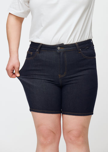 Plus-size modell sträcker mörkblå denimshorts för dam i färgen Midnights vid låret för att visa stretch.
