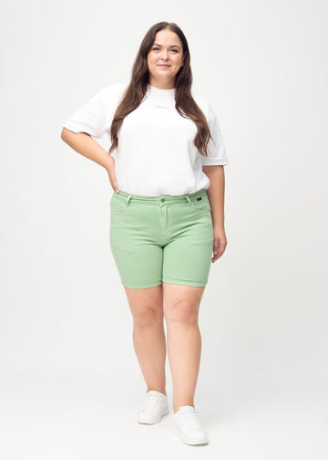 Helbild av en plus-size-modell i ljusgröna skinny short shorts.