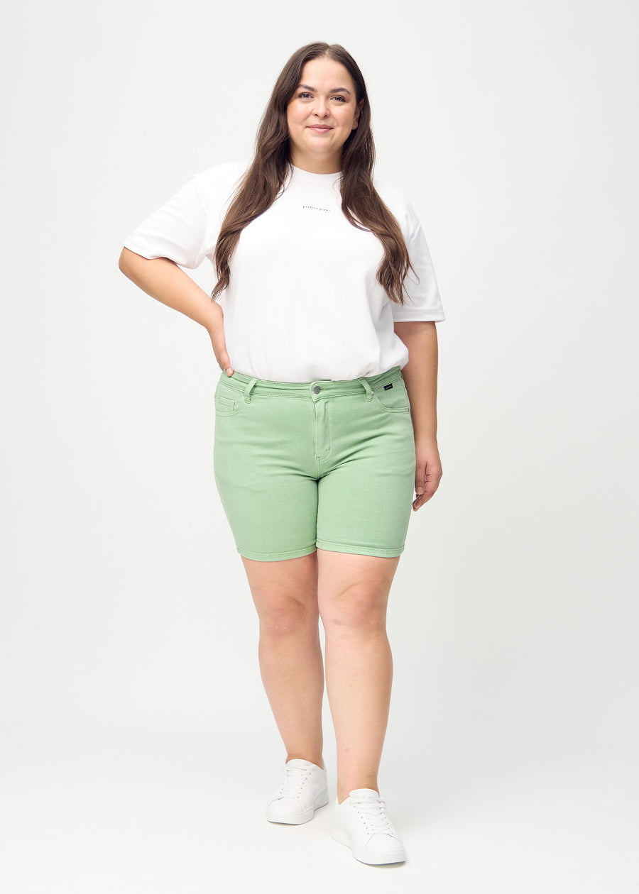 Helbild av en plus-size-modell i ljusgröna skinny short shorts.