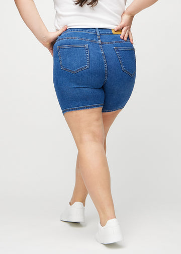 Mörk denim skinny short shorts sedda bakifrån på en plus-size-modell, så att man kan se hela produkten.