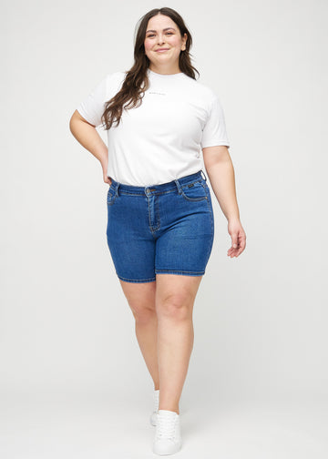 Helbild av en plus-size-modell i mörk denim skinny short shorts.