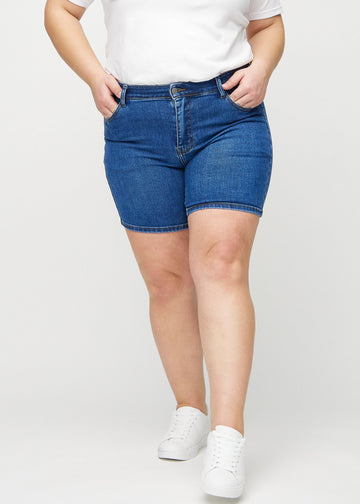 Mörk denim skinny short shorts, modellnamn Oceans, som sitter tight och slutar mitt på låret på en plus-size-modell, framifrån.