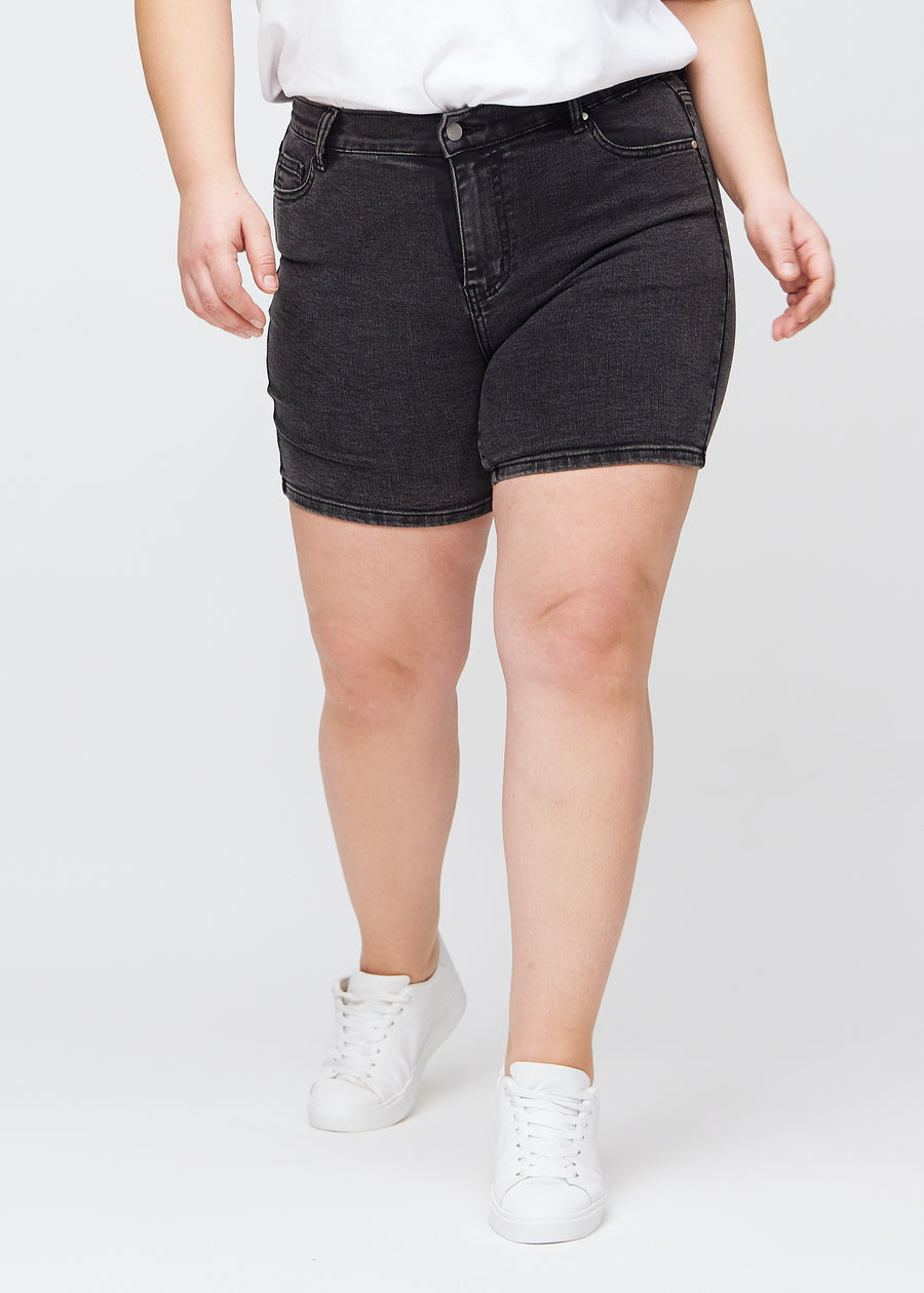 Mörkgrå denim skinny short shorts, modellnamn Shadows, som sitter tajt och slutar mitt på låret på en plus size-modell, framifrån.