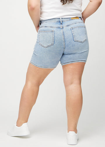 Ljus denim skinny short shorts sedda bakifrån på en plus size-modell, så att man kan se hela produkten.