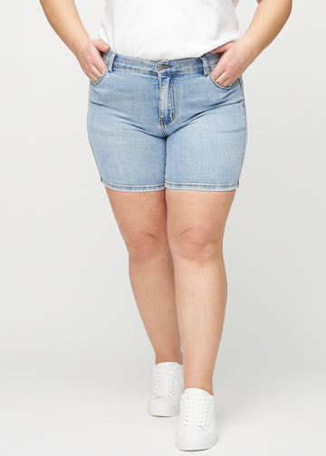 Ljus denim skinny short shorts, modellnamn Waves, som sitter tajt och slutar mitt på låret på en plus size-modell, framifrån.