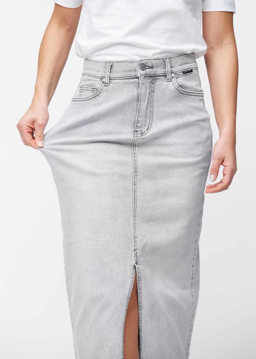 Lång ljusgrå denimkjol för kvinnor i färgen Ashes. En modell drar i tyget vid höften för att visa stretchen.