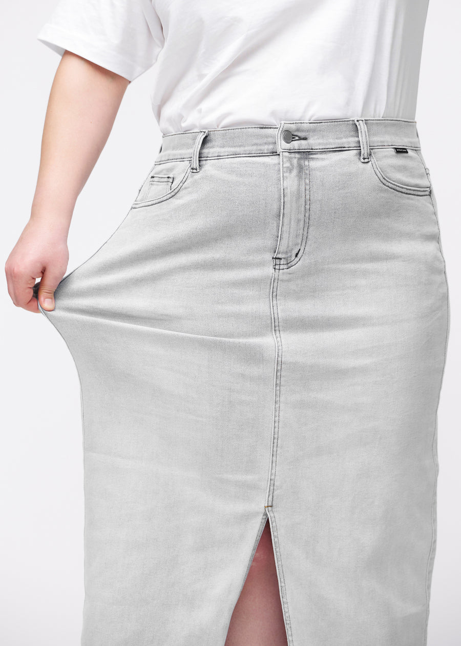 Lång ljusgrå denimkjol för kvinnor i färgen Ashes. En plus size-modell drar i tyget vid höften för att visa stretchen.