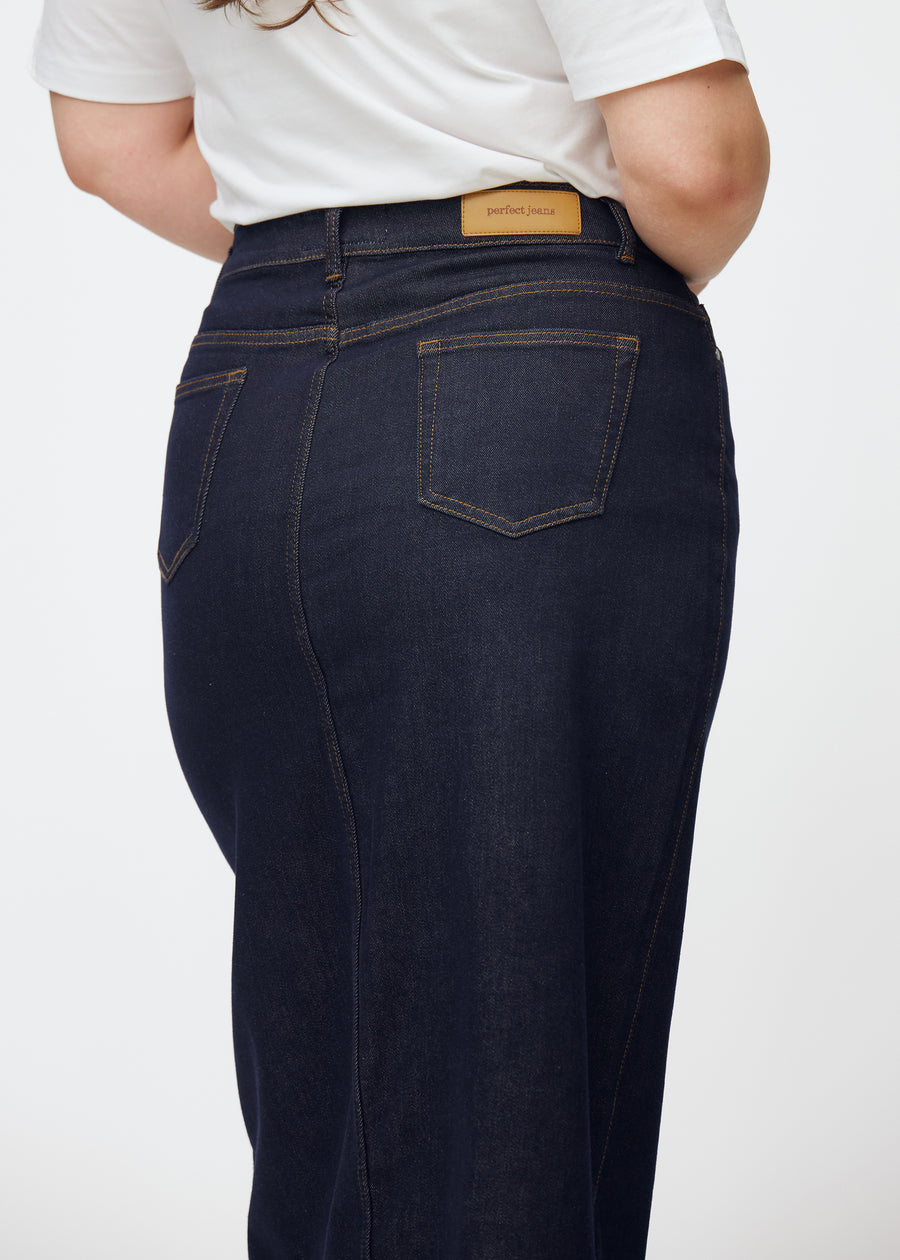Lång mörkblå denimkjol för dam i färgen Midnights sett bakifrån i närbild på plus-size modell för att visa passform och detaljer.