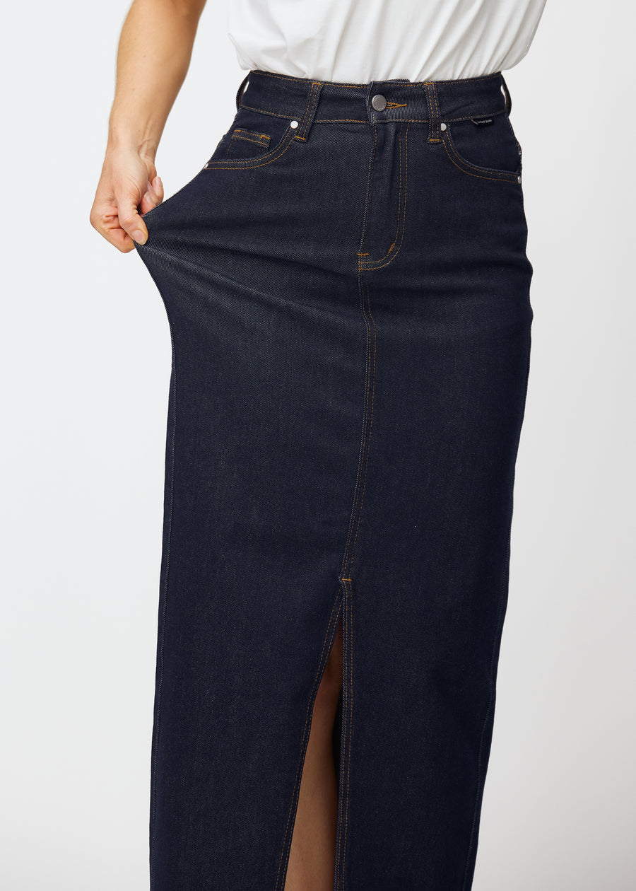Modell sträcker den långa mörkblå denimkjolen för dam i färgen Midnights vid höften för att visa materialets stretch.