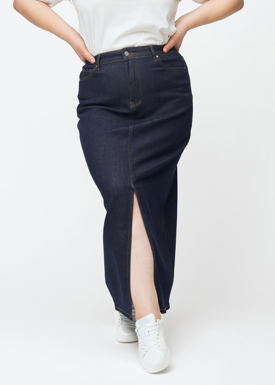 Lång mörkblå denimkjol för dam i färgen Midnights sett framifrån på plus-size modell, med slits framtill som börjar strax under knät.