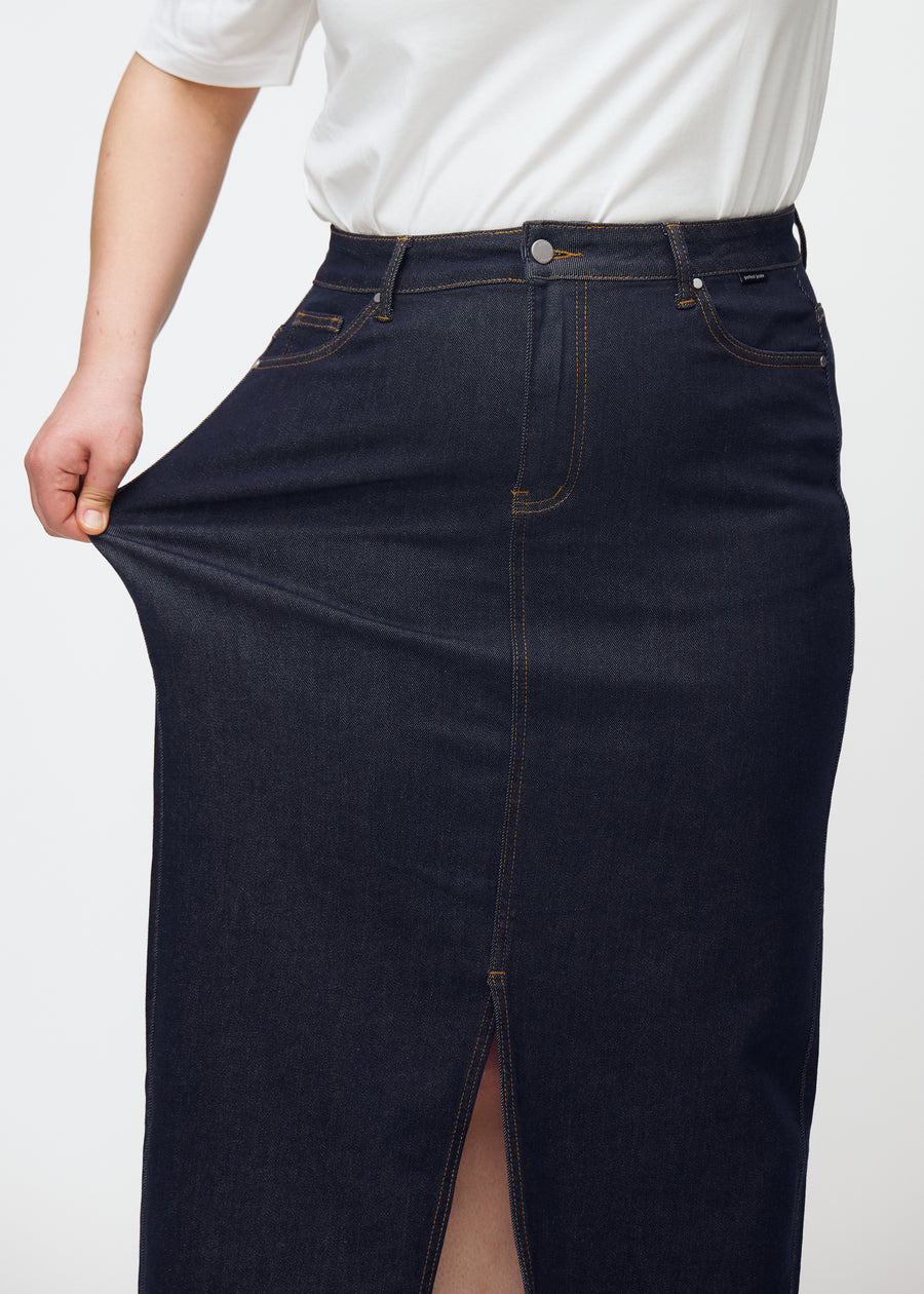 Plus-size modell sträcker den långa mörkblå denimkjolen för dam i färgen Midnights vid höften för att visa stretch.