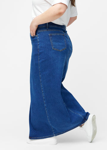 Lang, mørkeblå denimnederdel i farven Oceans med regulær pasform set fra siden på plus-size model, med synligt slids foran.