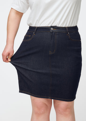 Plus-size modell sträcker mörkblå denimkjol för dam i färgen Midnights vid låret för att visa stretch.