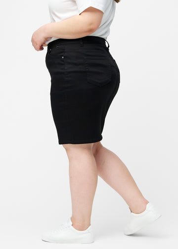 Sort, tætsiddende og knælang jeansnederdel set fra siden på plus-size model.