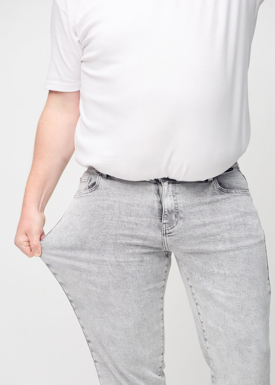 Plus size-modellen sträcker ut jeansen vid låret för att visa stretch.