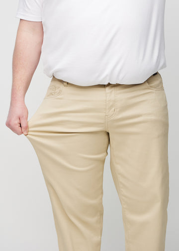 Plus size-modell drar i jeansen vid låret för att visa materialets stretch.