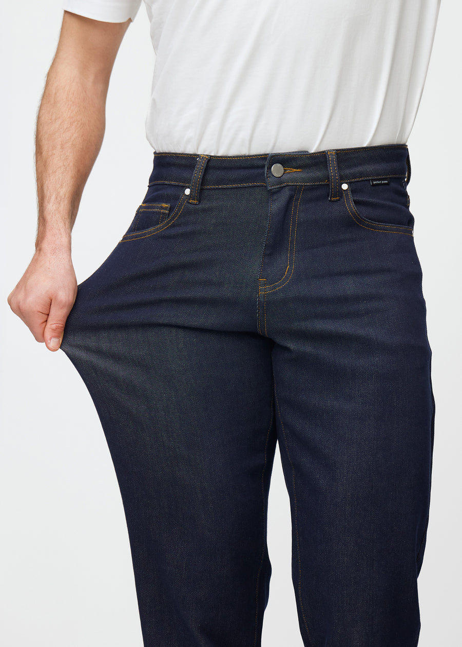 Modellen sträcker djup mörkblå denim jeans för män i färgen Midnights vid låret för att visa materialets stretch.
