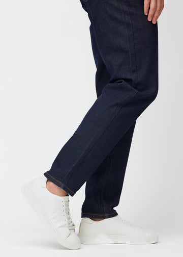 Djup mörkblå denim jeans för män i färgen Midnights med regular passform sedd på nära håll vid anklarna för att visa det raka avslutet.