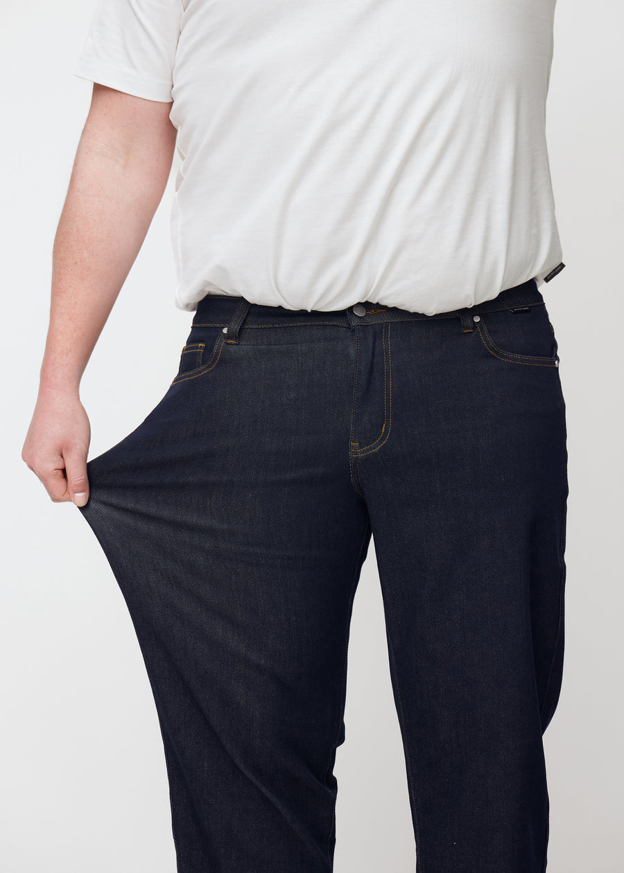 Plus-size-modell sträcker djup mörkblå denim jeans för män i färgen Midnights vid låret för att visa materialets stretch.