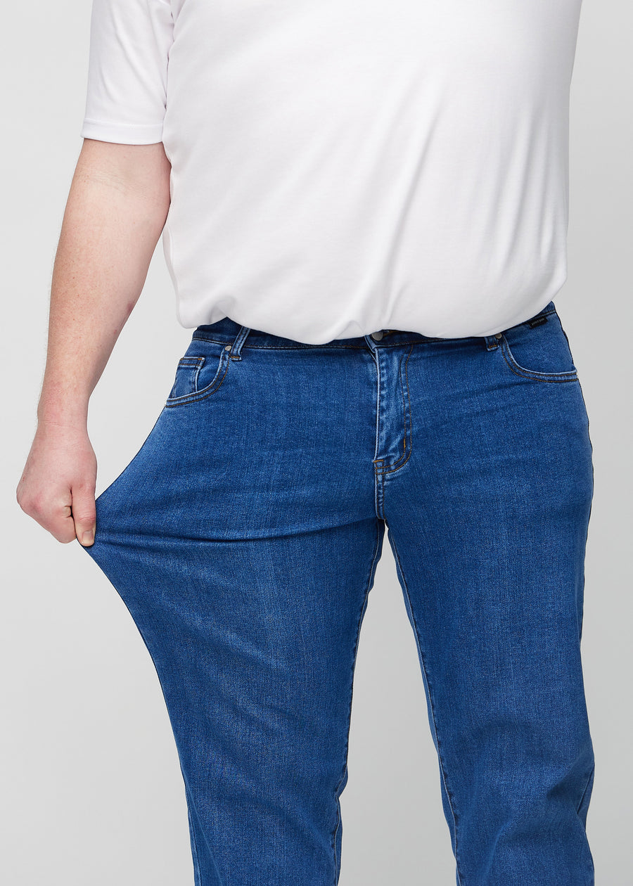 Plus-size-modellen sträcker jeansen vid låret för att visa stretch.