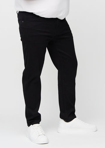 Svarta regular jeans, modellnamn Ravens, som går rakt ner längs benet på en plus-size-modell, sett framifrån.
