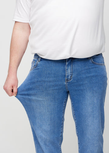 Plus size-modell drar ut jeansens tyg vid låret för att visa stretchen.