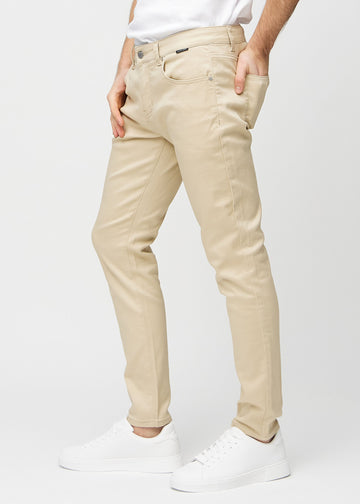 Beige jeans i slim fit sedda från sidan på en modell.
