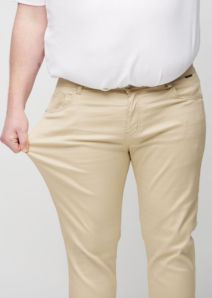 Plus size-modell drar i jeansen vid låret för att visa materialets stretch.