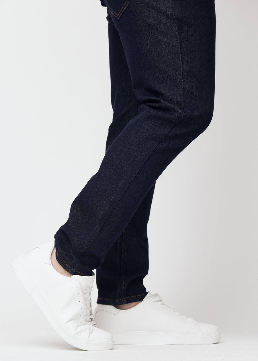 Djupt mörkblå denim jeans för män i färgen Midnights med slim passform sedd i närbild vid anklarna på plus-size-modell för att visa den smala avslutningen.
