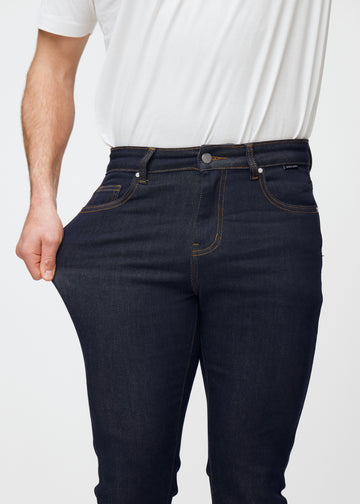 Modellen sträcker djupt mörkblå denim jeans för män i färgen Midnights vid låret för att visa materialets stretch.