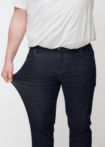 Plus-size-modell sträcker djupt mörkblå denim jeans för män i färgen Midnights vid låret för att visa materialets stretch.