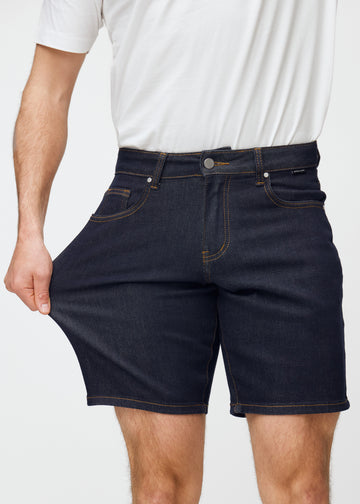 modell sträcker mörkblå denimshorts för herr i färgen midnights vid låret för att visa materialets stretch.