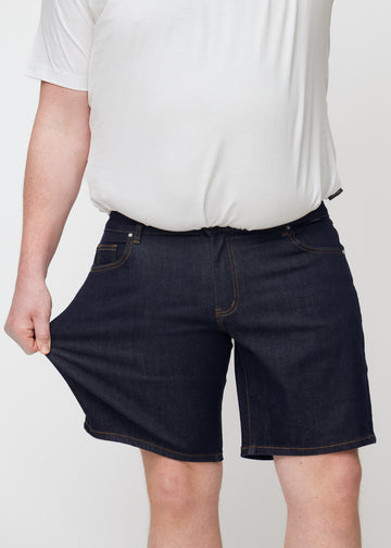 plus-size modell sträcker mörkblå denimshorts för herr i färgen midnights vid låret för att visa stretch.