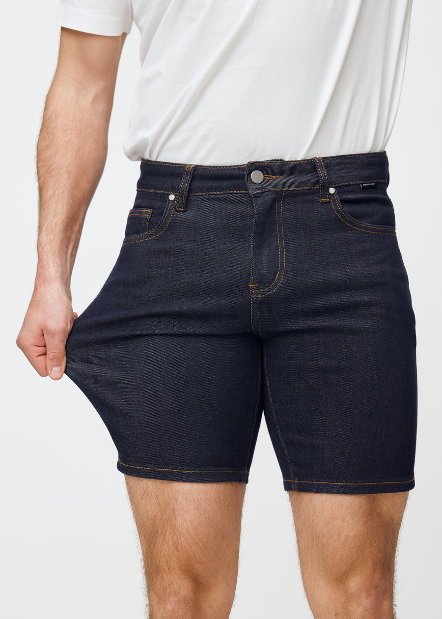 Modell sträcker mörkblå denimshorts för herr i färgen Midnights vid låret för att visa materialets stretch.