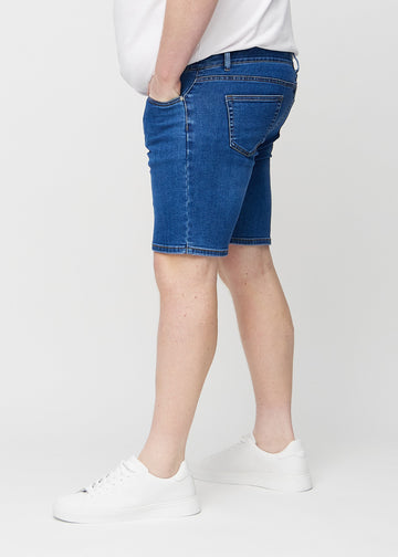 Mörka denim middle-slim shorts sedda från sidan på en plus size-modell.