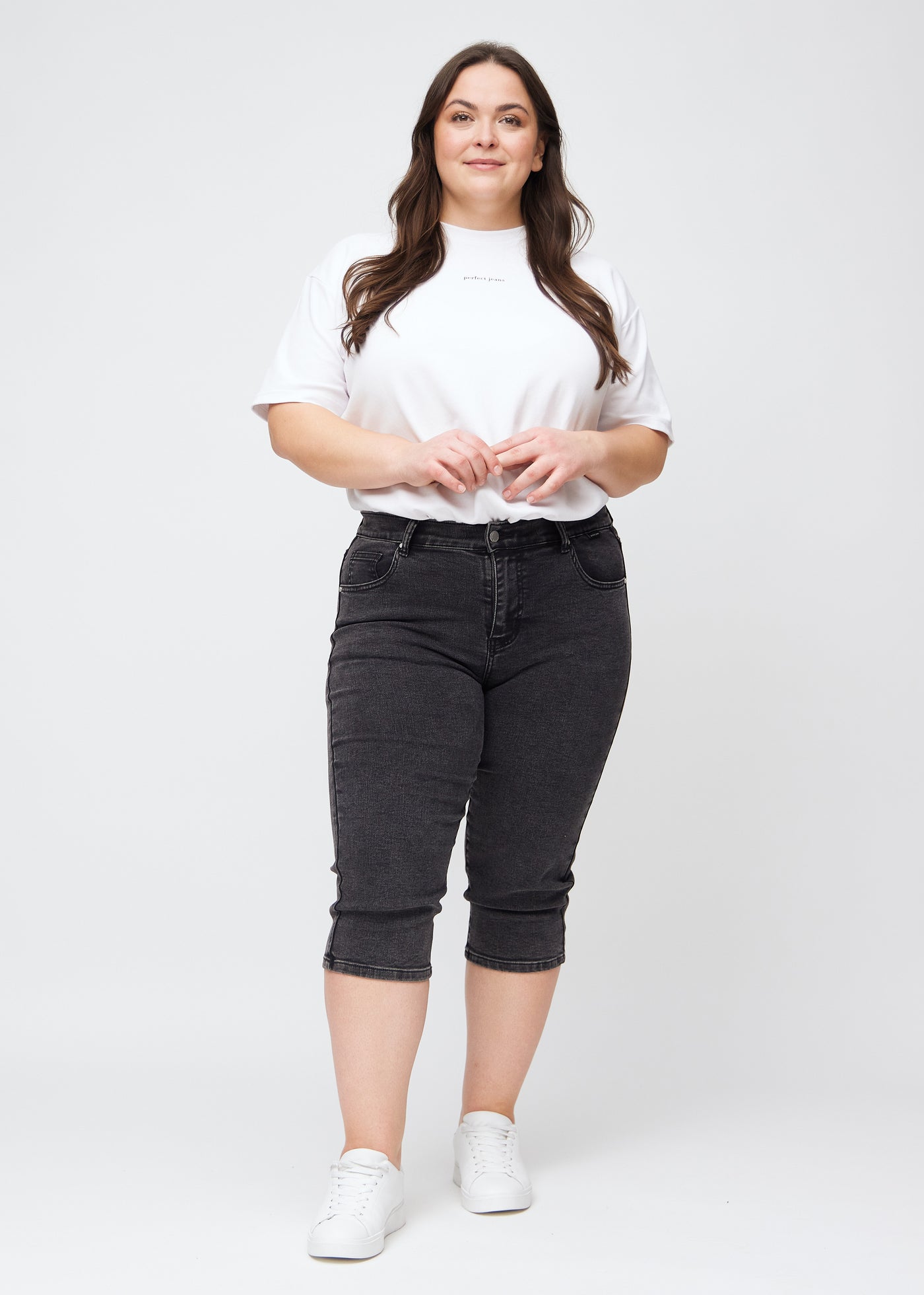 Plus-size model går ind i billedet, strækker i sine mørkegrå denim slim capris, drejer rundt for at vise dem frem og forlader derefter billedet.