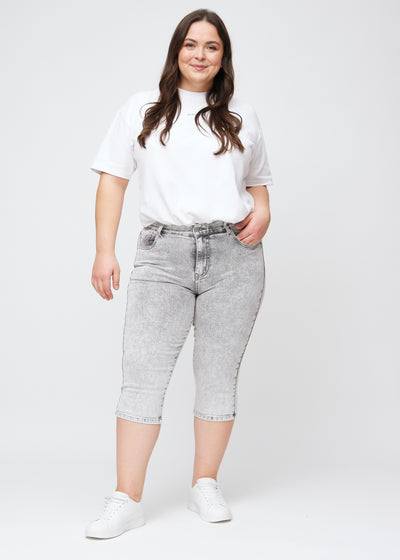 Plus-size model går ind i billedet, strækker i sine lysegrå denim slim capris, drejer rundt for at vise dem frem og forlader derefter billedet.
