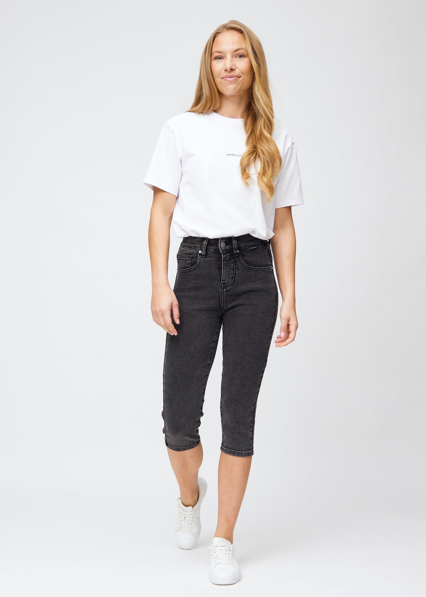 Model træder ind i billedet, strækker i sine mørkegrå denim slim capris, viser dem frem ved at dreje rundt, og går derefter ud af billedet igen.